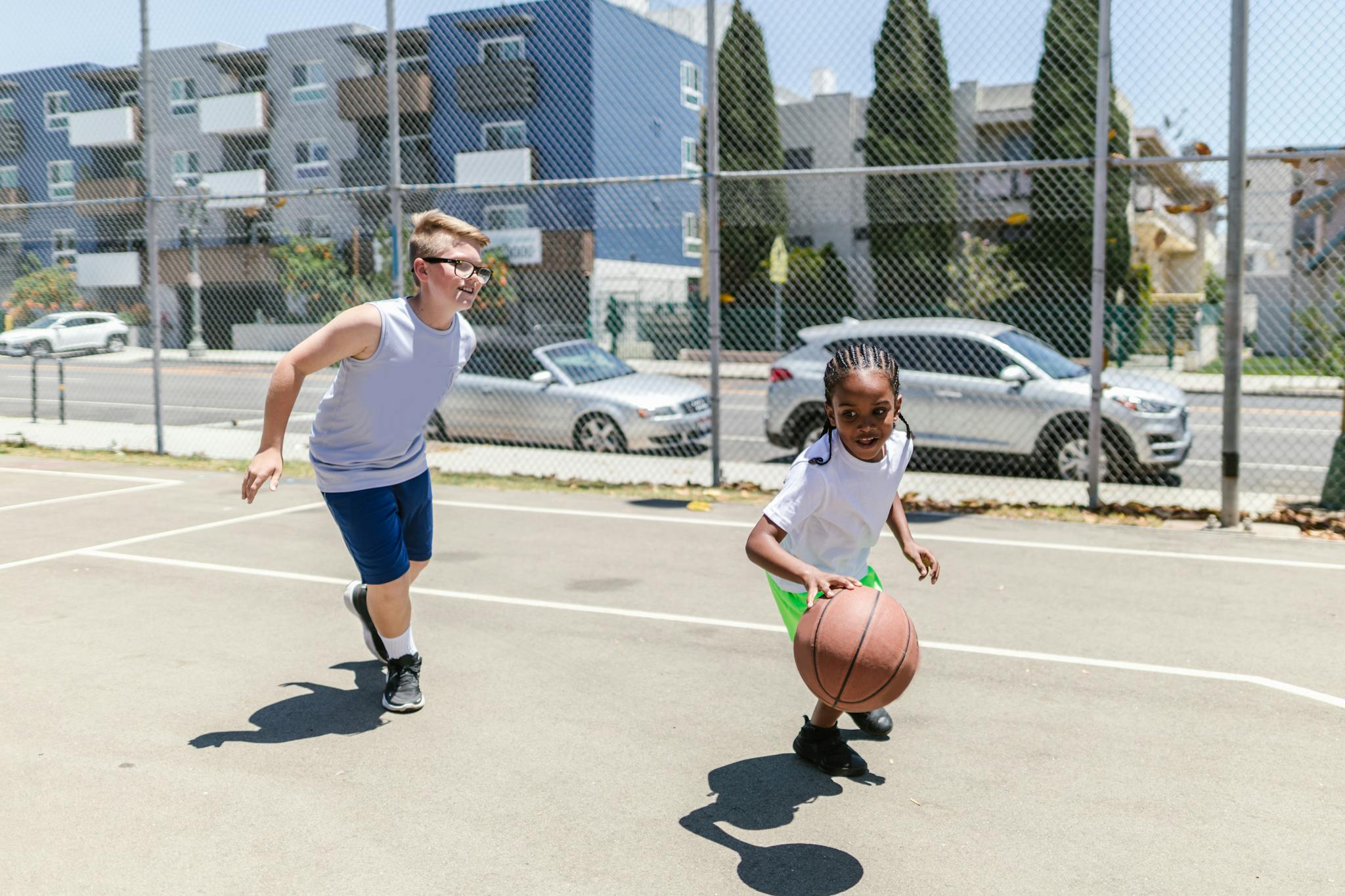 Kids enjoying a game of basketball on a sunny day on an urban outdoor court.