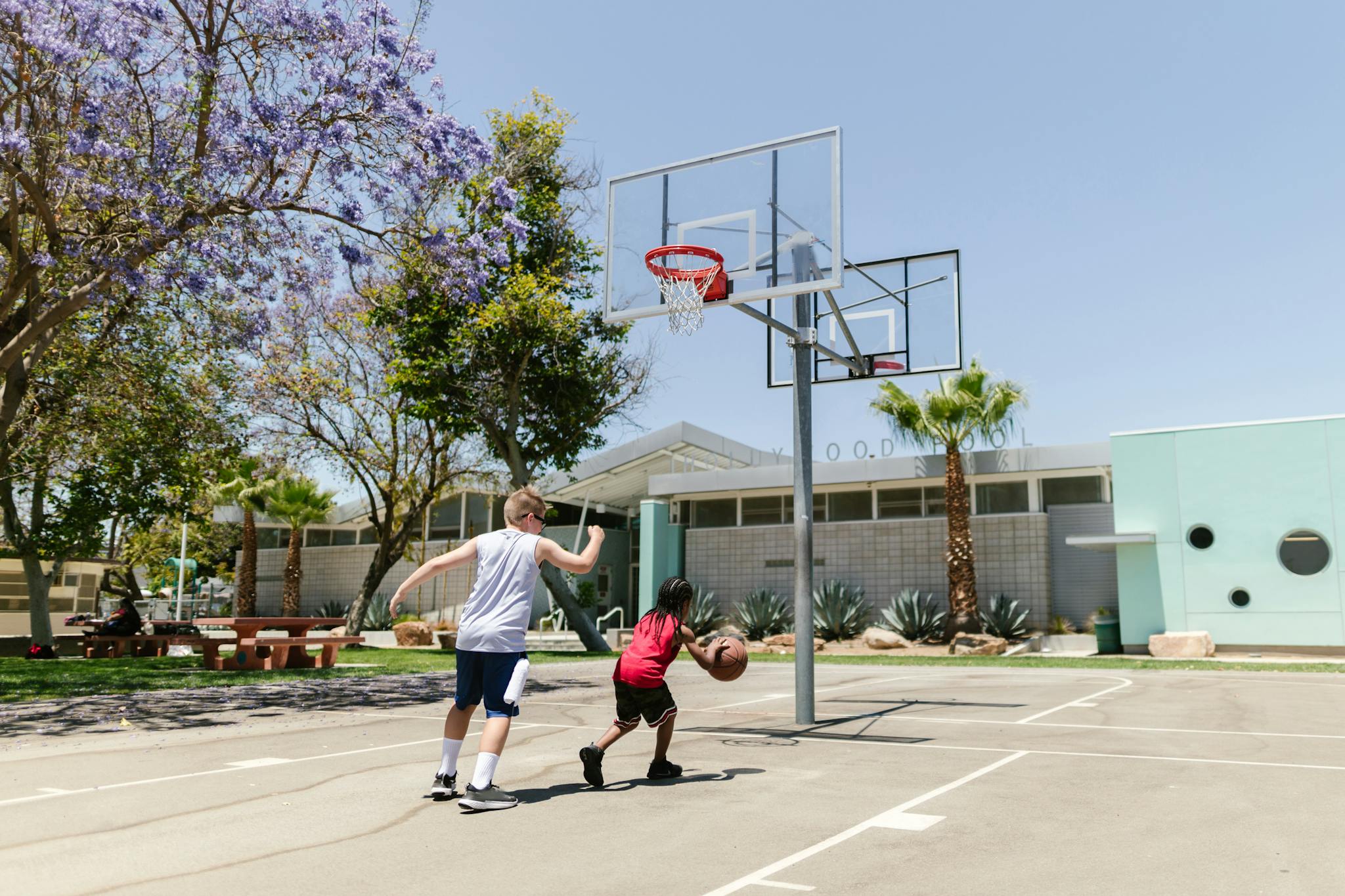 Two boys playing basketball outdoors on a sunny day at school court.