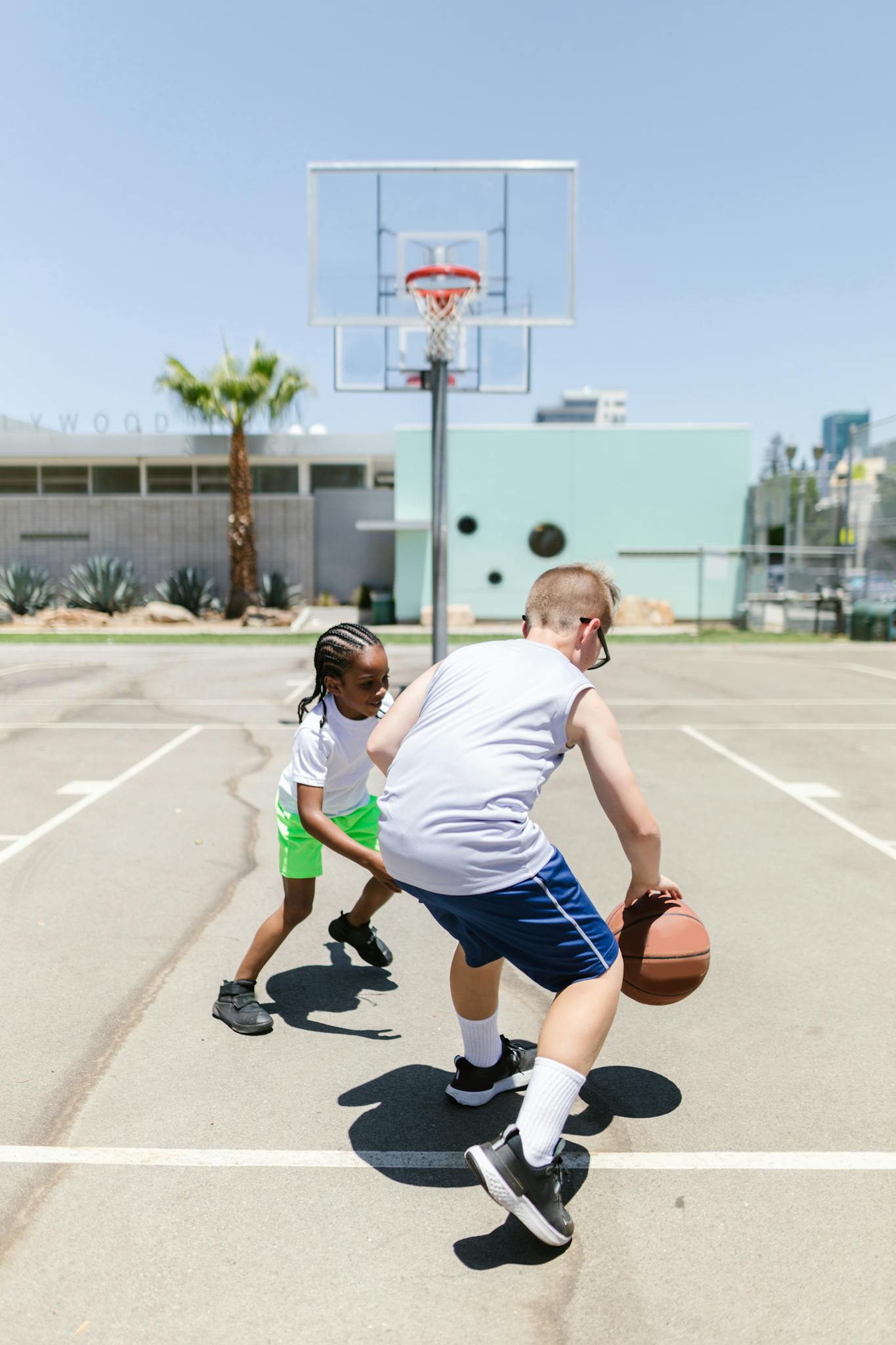 Two young boys playing basketball on an outdoor court during the day.